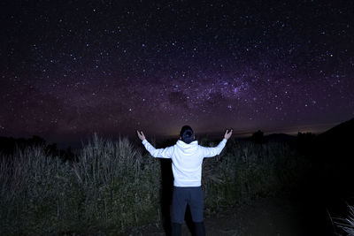 Rear view of man with arms outstretched standing at night