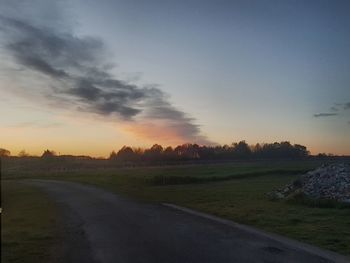 Road amidst field against sky during sunset