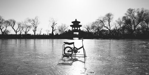 Bicycle on frozen lake against silhouette bridge