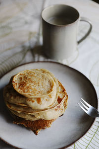 From above plate with fresh pancakes placed near mug of hot beverage