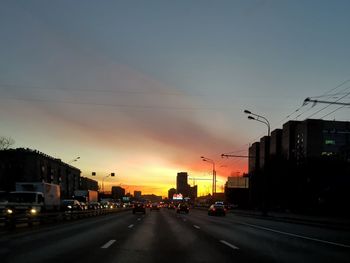 Cars on city street against sky at sunset