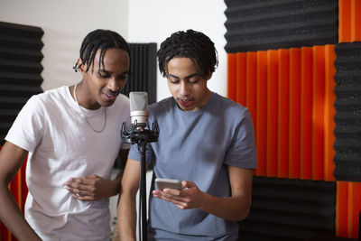 Teenage rappers sharing smart phone while recording song in studio