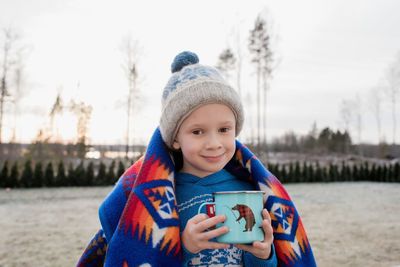 Young boy smiling whilst wrapped in a blanket holding a hot chocolate