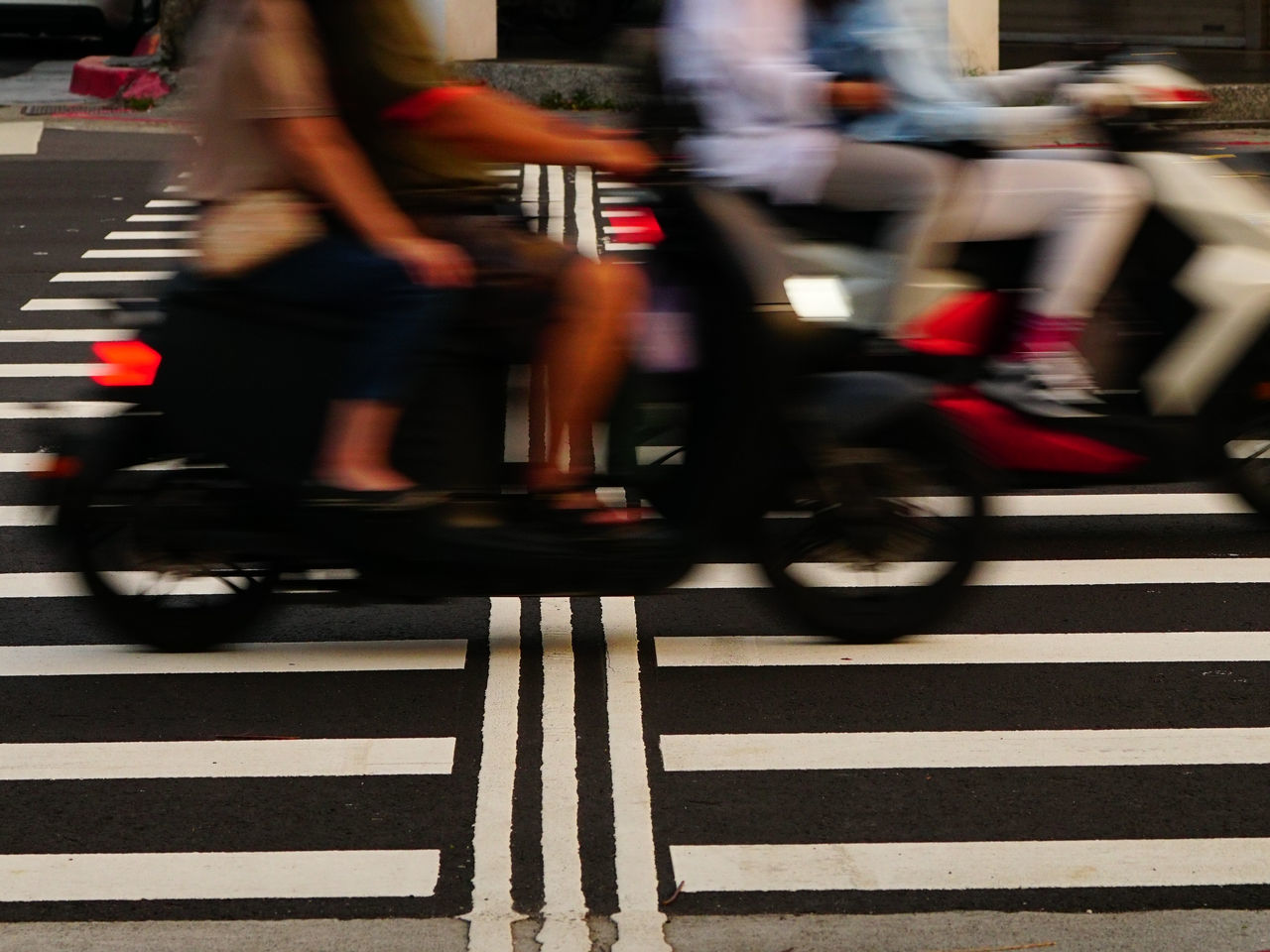 blurred motion, transportation, motion, crosswalk, zebra crossing, crossing, city, road marking, speed, road, street, mode of transportation, city life, marking, group of people, city street, pedestrian crossing, architecture, symbol, on the move, sign, bicycle, traffic, adult, men, clothing, striped, commuter, activity, low section, vehicle, walking, human leg, travel, outdoors, lifestyles, red, person, women, footwear, land vehicle, crowd, cycling, infrastructure, wheel, sports, limb