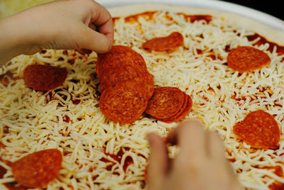 Cropped hand of person placing pepperoni on pizza