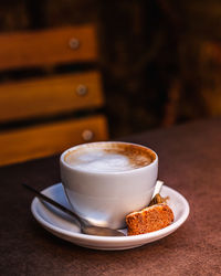 Close-up of coffee cup with biscuit on table