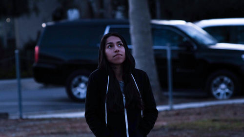 Young woman looking up while standing against car