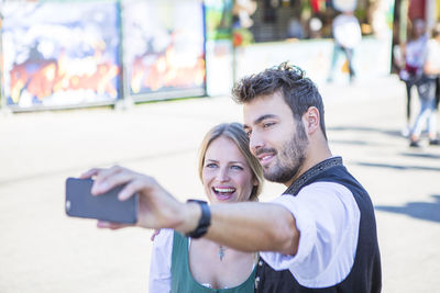 Smiling man and woman taking selfie while standing on street at event