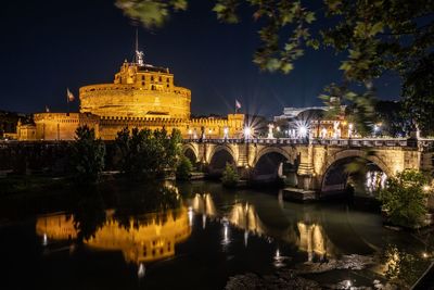 Illuminated bridge over river against buildings at night