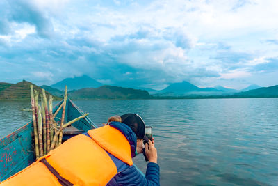 Rear view of man standing by lake against sky
