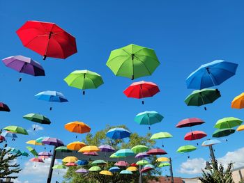 Low angle view of umbrellas hanging against clear blue sky