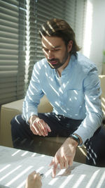 Young man looking down while sitting on table