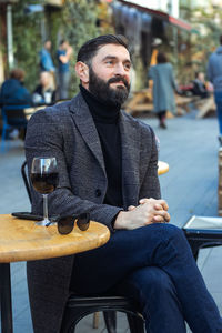 Brutal bearded middle-aged man in a street cafe with a glass of wine