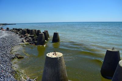 Wooden posts in sea against clear blue sky