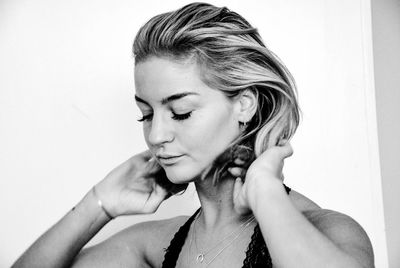 Close-up of woman with hand in hair standing against white background