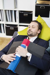 Mid adult businessman with folder sleeping on sofa in office