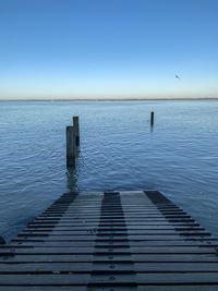 Wooden posts in sea against clear blue sky