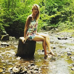 Full length of young woman sitting against trees