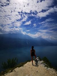 Rear view of woman standing by cliff while looking at mountain against sky