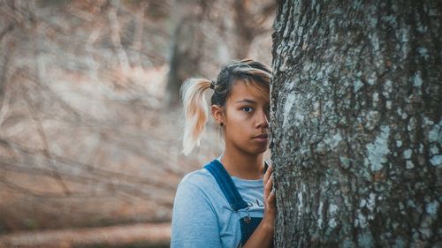 Portrait of young woman standing by tree