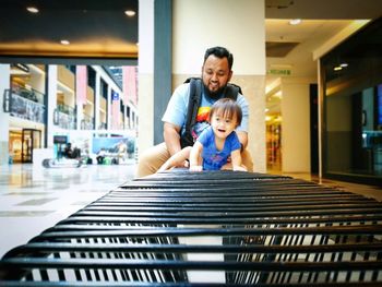 Father sitting with baby girl on metal railing in shopping cart