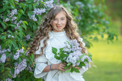 Portrait of smiling woman with flower bouquet against plants