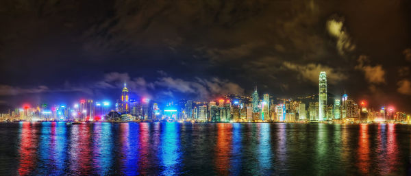 Illuminated city by river against sky at night