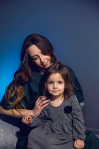 Mother and daughter in dresses sitting on a bed in a bedroom with a blue wall