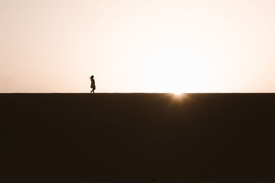 Silhouette of man standing on beach against sky during sunset