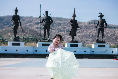 Portrait of young woman standing with umbrella against sky