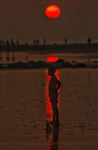 Silhouette man standing on beach against sky during sunset