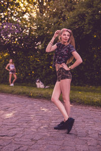 Full length of young woman standing on footpath against trees at park