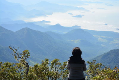 Rear view of woman sitting on mountain against sky