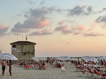 People at beach against sky during sunset