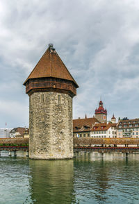 Old building by river against cloudy sky