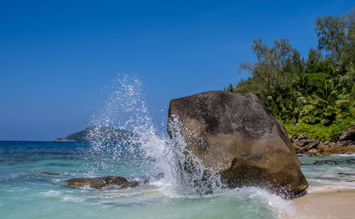 Water splashing on rocks by sea against clear blue sky