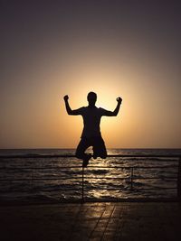 Silhouette man jumping at beach against sky during sunset