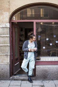 Smiling young female potter standing with coffee cup at doorway of ceramics store