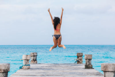 Rear view of woman jumping on pier against sky