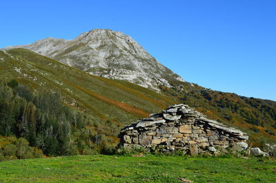 House on field by mountain against clear sky