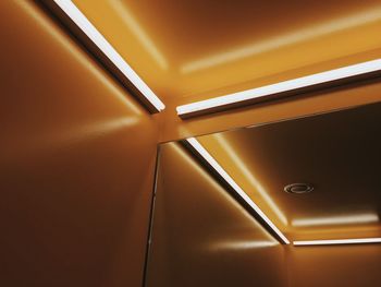 Low angle view of illuminated fluorescent lights with reflection in mirror