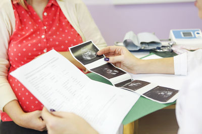 Midsection of doctor holding ultrasound photographs with patient in hospital