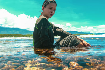 Young woman sitting by sea against sky