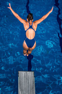 Rear view of mid adult woman with arms outstretched jumping from diving platform in swimming pool