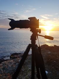 Silhouette man photographing at beach against sky during sunset