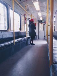 Rear view of woman in warm clothing standing in train