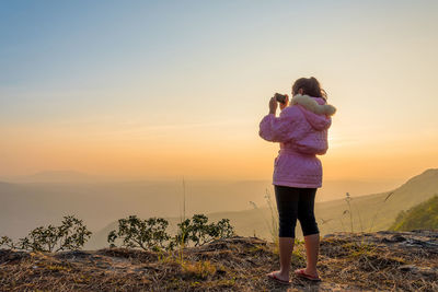 Rear view of woman photographing against sky during sunset