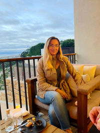 Portrait of young woman sitting on chair against sea