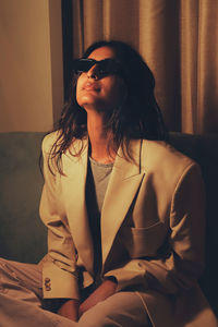 Portrait of young woman wearing sunglasses standing against curtains 