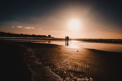 Silhouette people standing at beach against sky during sunset